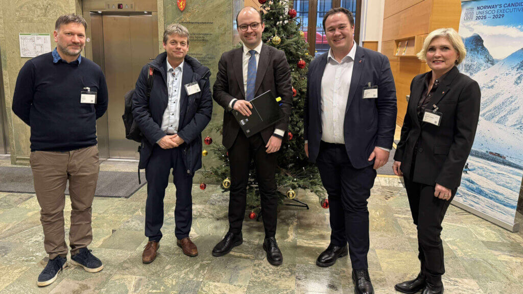 Foto av 5 personar som står i ein vestibyle, bak dei eit pynta juletre.