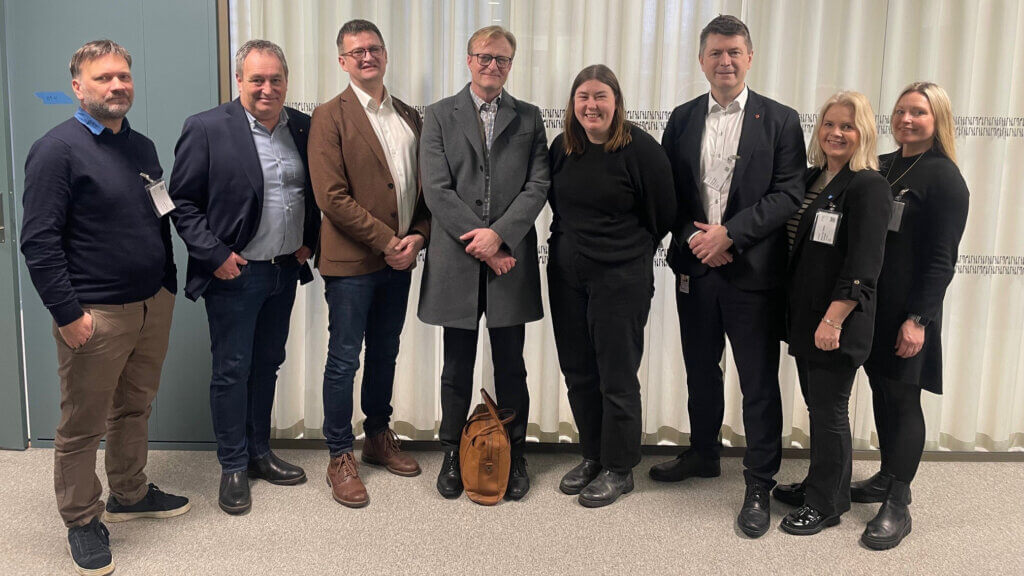 Foto av 8 personar som står i eit kontorbygg, innandørs.