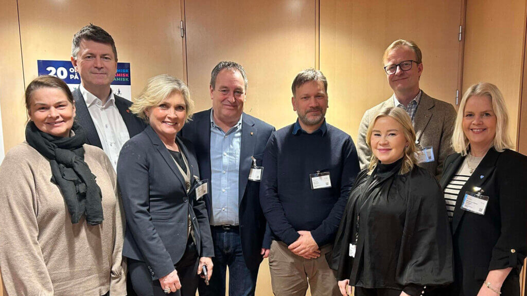 Foto av 8 personar som står foran dørar, innandørs.