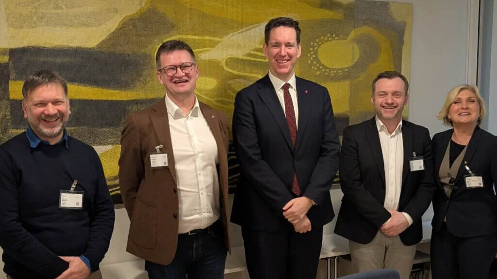 Foto av 5 personar som står foran eit veggmaleri.