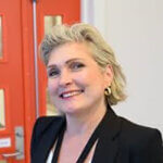 Bilde av konstituert kommunedirektør i Stord kommune, Mariann Jacobsen Hilt, iført svart dressjakke, står foran raud dør